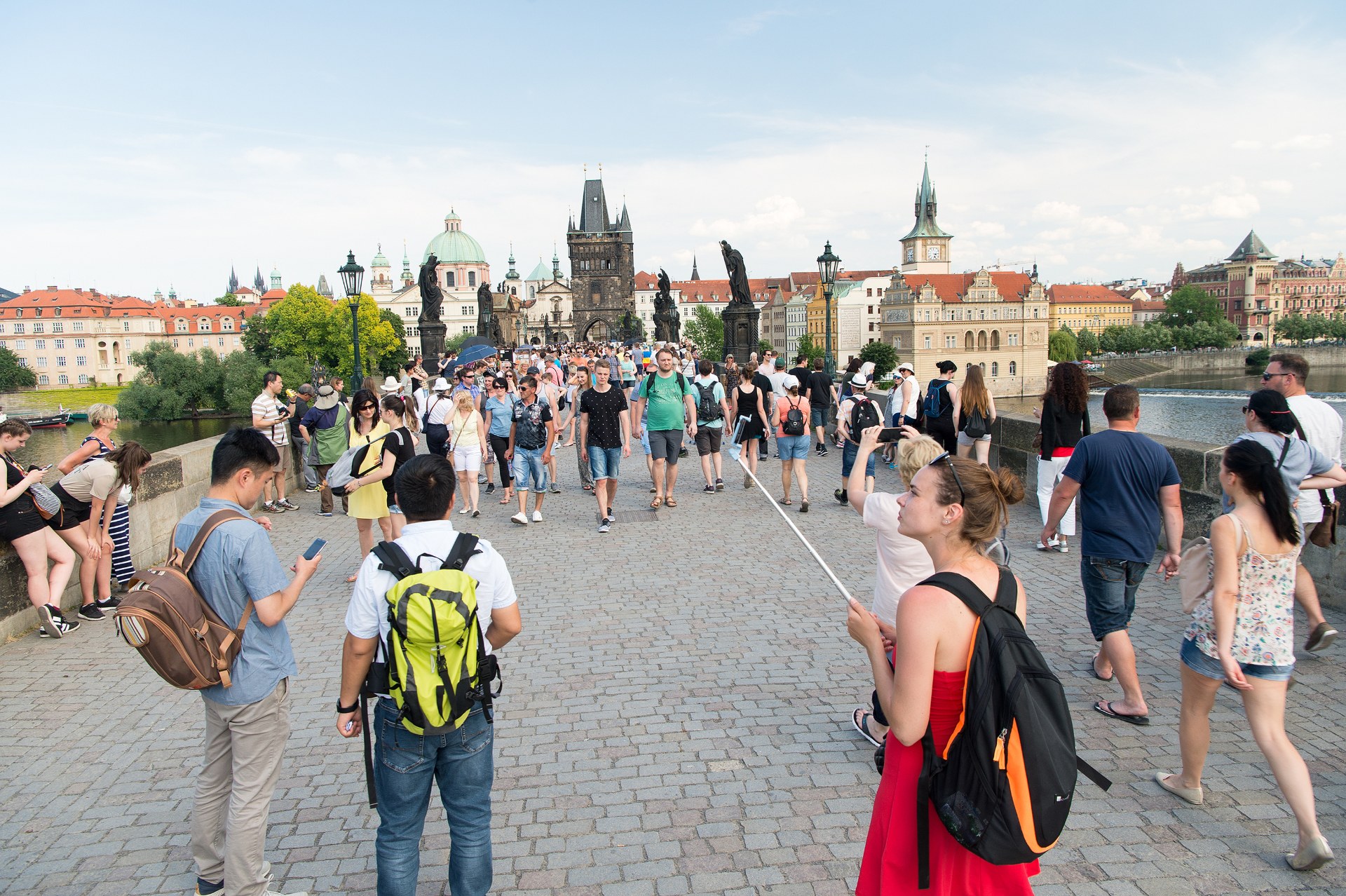 Jóvenes con mochilas cruzando el Puente de Carlos en Praga, con la torre del puente de la Ciudad Vieja al fondo